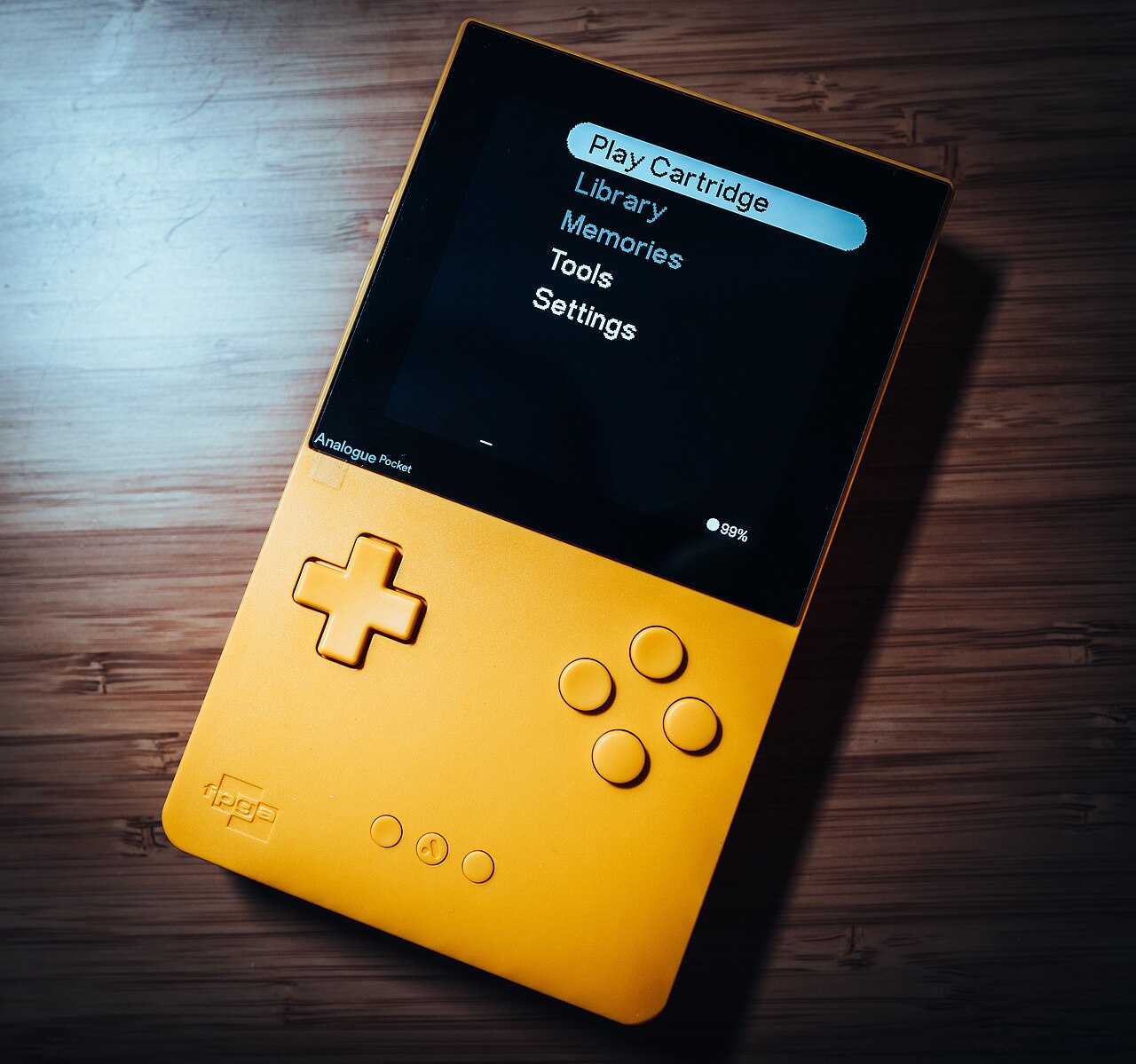 A yellow Analogue Pocket handheld on a wooden surface, showing the Analogue OS menu on its bright display